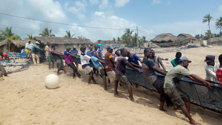 A group of men dragging a boat onto the beach.